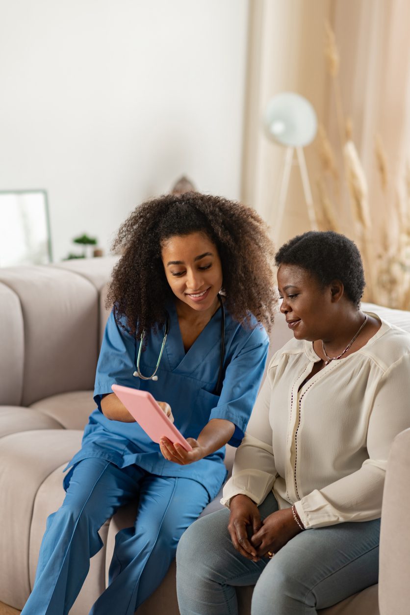 Pleasant curly nurse showing online news to elderly lady Home Health Care Marketing